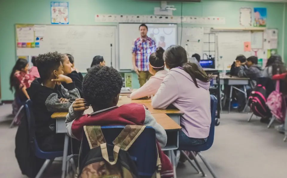 Students at desks watching a teacher present in a classroom